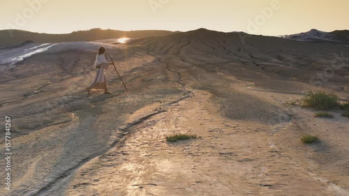 Jesus walking in the desert over patches of grass, with the sun setting�behind�Him.