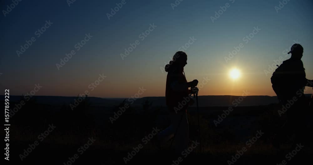 Silhouettes of a man and a woman walking with backpacks and walking poles against the backdrop of a sunset. Silhouettes of a man and a woman walking with backpacks and walking poles against the backdrop of a sunset.