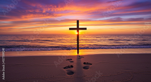 Fototapeta Naklejka Na Ścianę i Meble -  Silhouette of a cross on a beach at sunset with footprints leading to it and colorful sky above