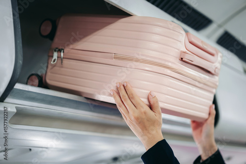 hands placing pink carry on luggage bag securely in overhead storage compartment airplane cabin preparing travel journey flight departure