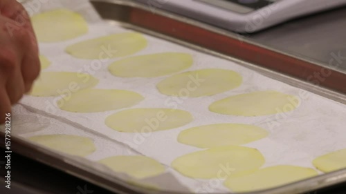 Wallpaper Mural Close-up of hands arranging thin, raw potato slices on a paper towel-lined baking sheet. This essential step prepares potatoes for frying or baking, ensuring crispy results and even cooking. Torontodigital.ca