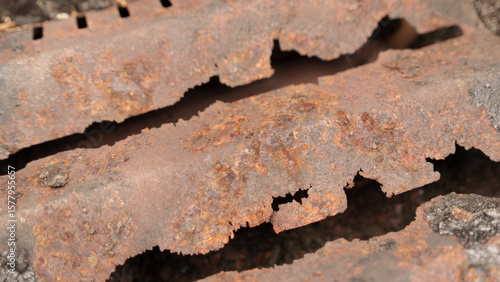 Detailed image showcasing a close-up view of a metal grate, heavily affected by rust and corrosion. The texture and earthy tones highlight the decay process.