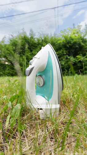 A sleek steam iron positioned upright in a grassy area, contrasting its modern design with the natural surroundings of lush green foliage and sky.