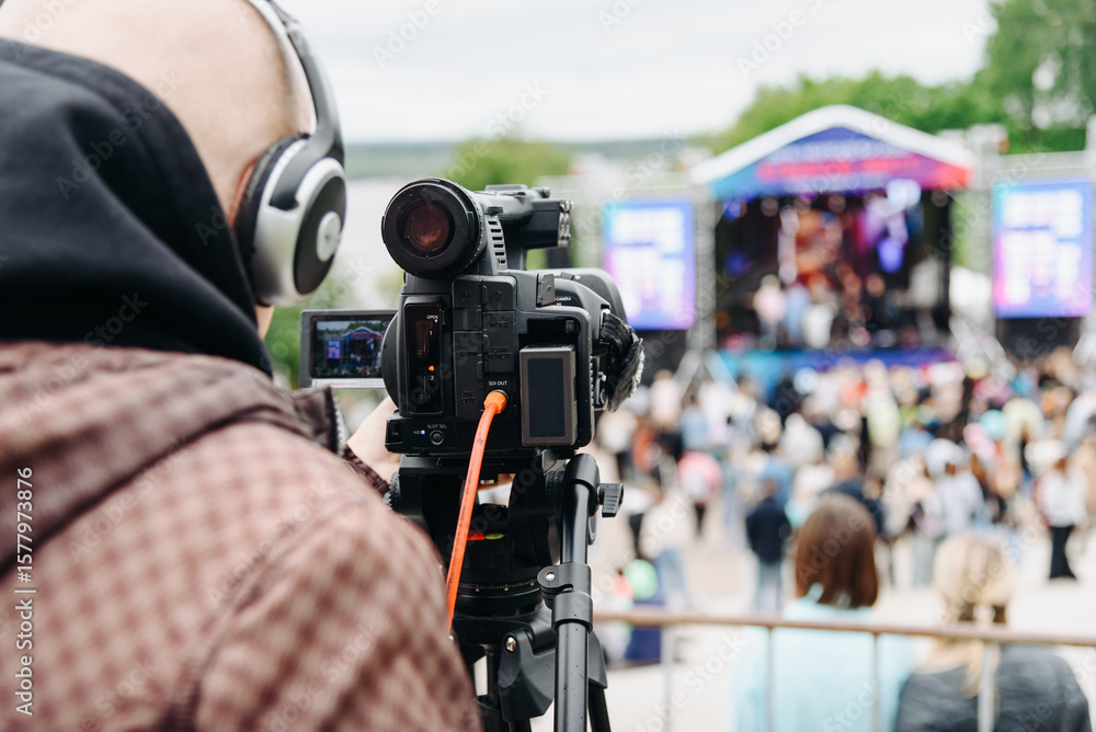 large black video camera on tripod outdoors, operator videographer shooting music festival and crowd of people outdoors, television work large black video camera on tripod outdoors, operator videographer shooting music festival and crowd of people outdoors, television work