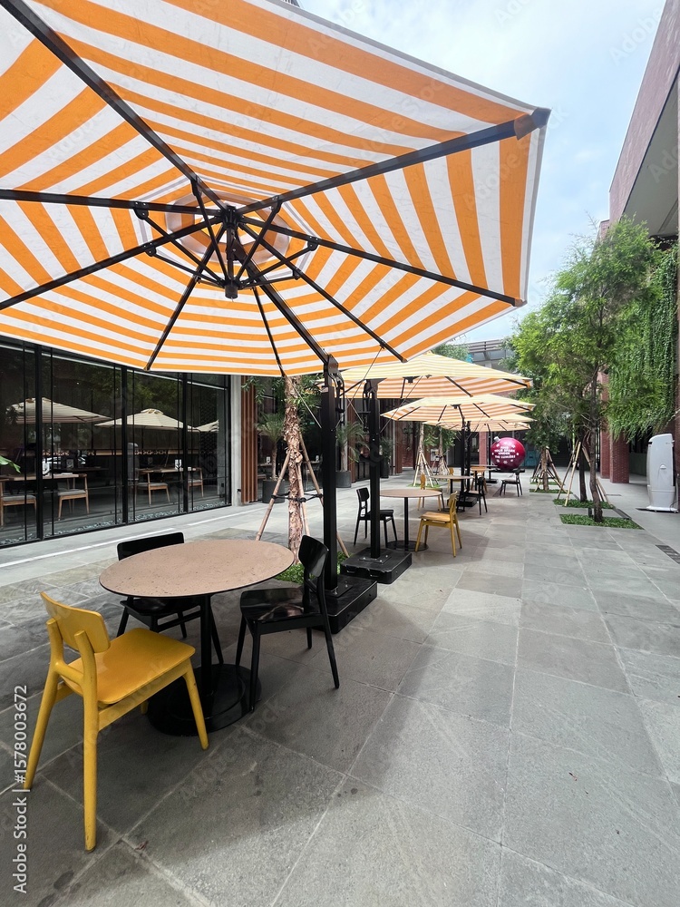 Fototapeta premium Sidewalk Cafe with Orange Striped Umbrellas on Grey Pavement