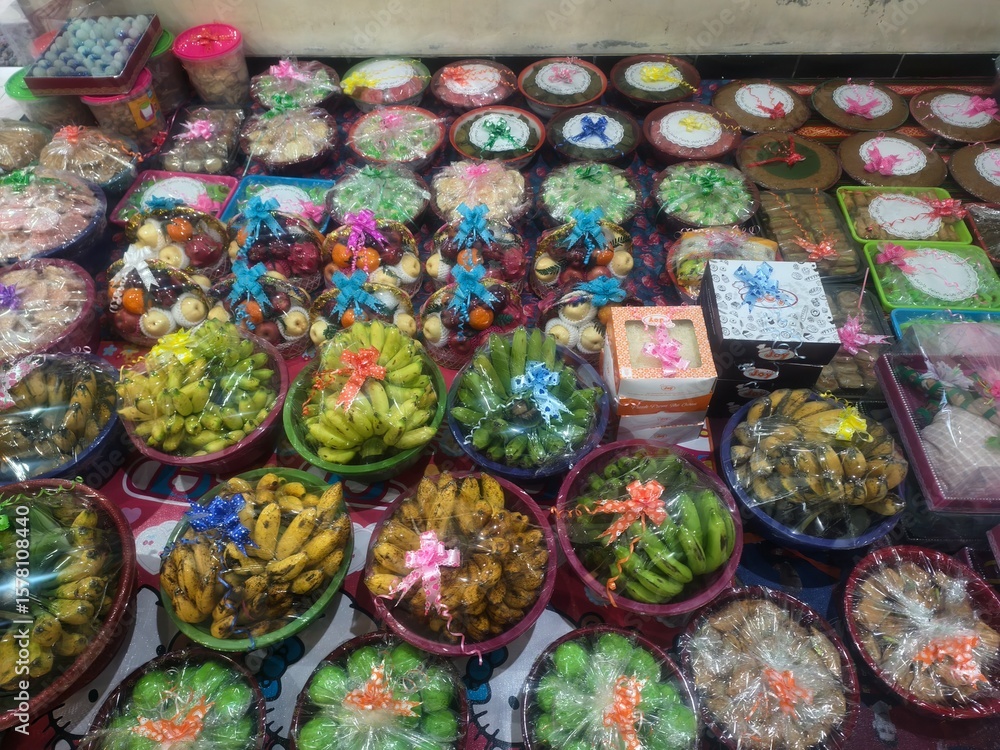 Fototapeta premium Assorted Fruits and Traditional Sweets in Decorative Packaging, Display of Festive Food Gifts Wrapped in Plastic and Tied with Ribbons
