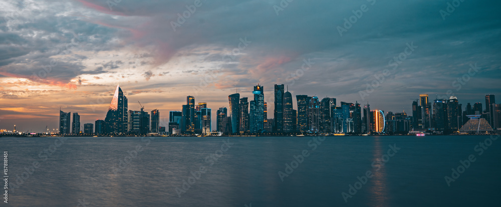 Obraz premium Panorama of Doha, capital of Qatar. View of Doha from the sea. Skyscrapers on a rose and blue background. Modern architecture of Doha at sunset in the evening, view from the sea.