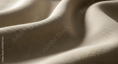 A close-up of textured beige fabric, showing soft folds and subtle variations in light and shadow across its surface.