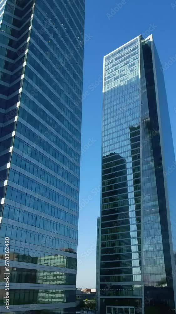 Two modern, blue glass skyscrapers soar against a clear sky, reflecting the surrounding urban landscape in their facade Two modern, blue glass skyscrapers soar against a clear sky, reflecting the surrounding urban landscape in their facade