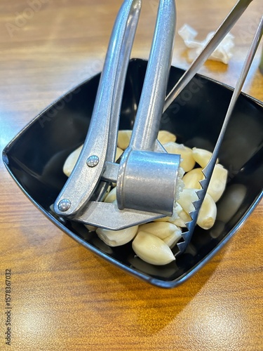 Fotografia peeled garlic on the black bowl with garlic presser on the top.