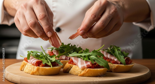 Chef prepares gourmet bruschetta with fresh arugula and prosciutto on toasted bread slices, carefully arranging ingredients for elegant appetizer presentation