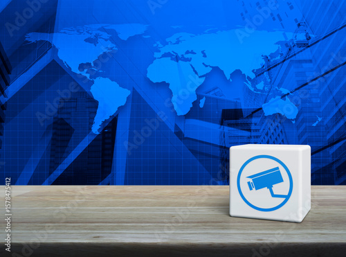 Fototapeta Naklejka Na Ścianę i Meble -  Cctv camera icon on white block cube on wooden table over world map, modern office city tower and skyscraper, Technology security and safety online concept, Elements of this image furnished by NASA