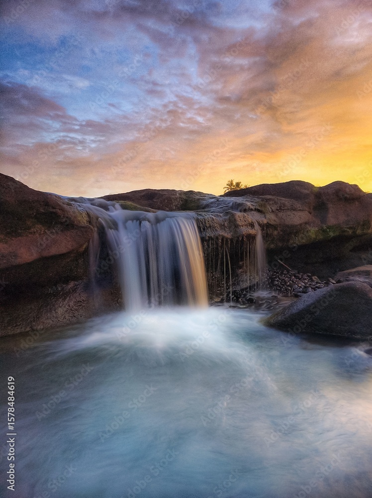 Fototapeta premium a waterfall that flows between black rocks and is illuminated by the afternoon sun