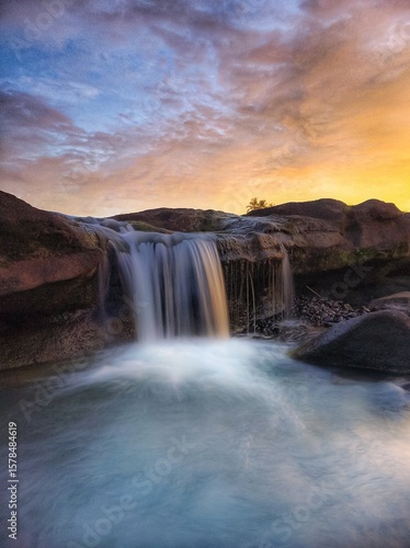 a waterfall that flows between black rocks and is illuminated by the afternoon sun