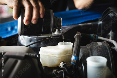 Auto mechanic adding brake fluid in brake fluid reservoir.