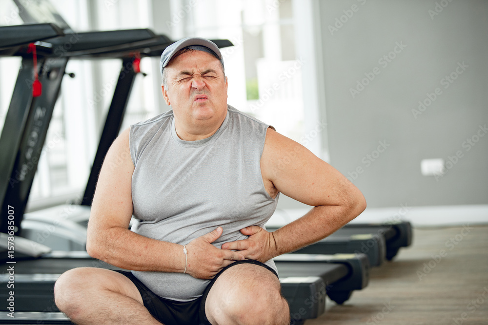 Obraz premium man at the gym with hand on stomach because nausea, painful disease feeling unwell. ache concept.