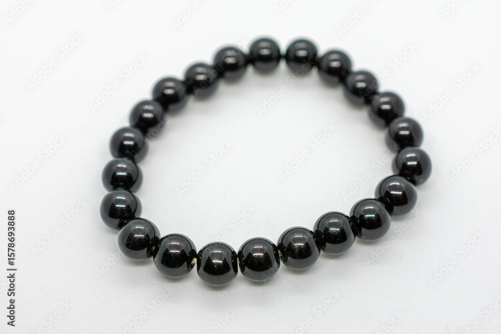 Obraz premium Black bracelet with a shiny surface. The bracelet is made of small black beads. The beads are arranged in a circular pattern. The bracelet is made of a shiny material that reflects light.