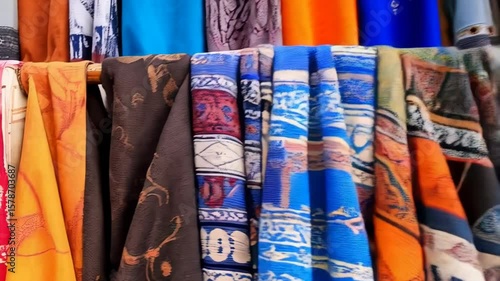 Colorful textile assortment showcases vibrant patterns and solid hues in retail display featuring variety of scarves and shawls hanging in market stall.