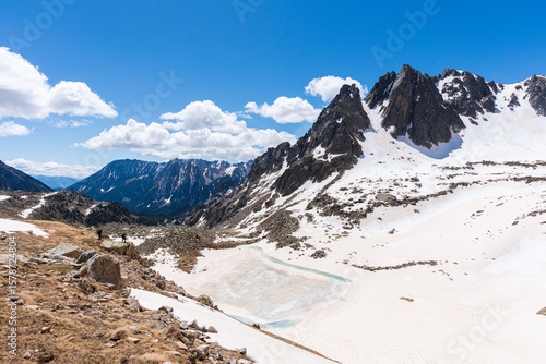 Majestic snowy mountains and a partially frozen lake in the Pyrenees, seen from the GR11 trail at Port de Ratera, Lleida. Clear sky and dramatic peaks in a pristine alpine setting.