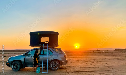 Car with rooftop tent with ladder stands against sunset background, camping