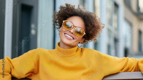 Cheerful outdoor fashion featuring bright smile, stylish sunglasses, and vibrant sweater ensemble