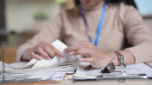 A woman is sitting at a desk with a stack of money in her hand. She is looking at the money and she is counting it