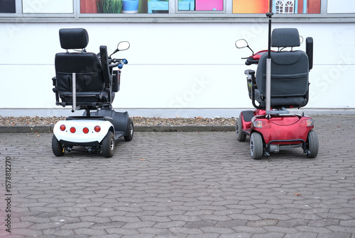 Konzept Alter, Überalterung, Mobilität und Gesellschaft im demografischen Wandel: Zwei Elektromobile mit Einkaufskorb parken nebeneinander vor einem Geschäft, viel Copyspace