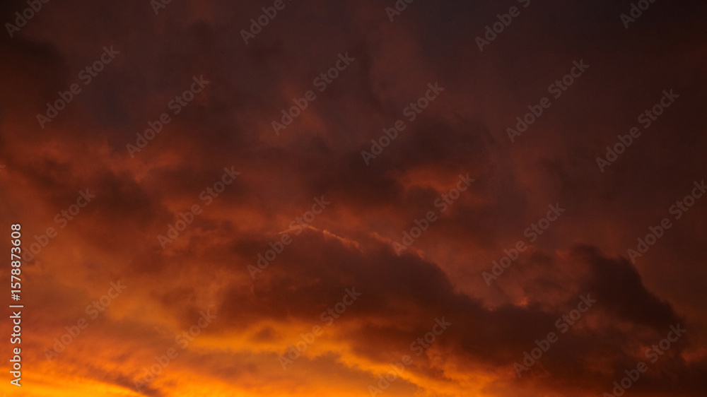 Naklejka premium Dramatic sunset sky with vibrant orange and purple hues, showcasing textured clouds illuminated by the fading light, creating a stunning natural atmosphere and visual spectacle