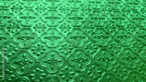 A close-up view of vibrant green translucent glass, patterned with intricate floral and geometric motifs.