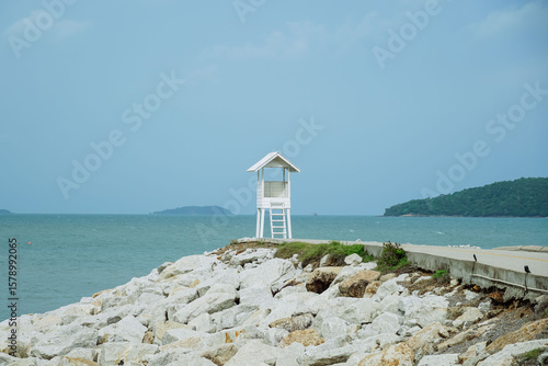 Small lighthouse on the shore of the sea at Khao Laem Ya, Rayong, Thailand. Little wooden white life guard tower. Summer travel vacation and holiday concept. Seascape Bridge and Pier.