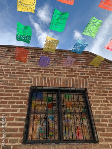 Wallpaper Mural Vibrant papel picado decorations hang above a brick building in a lively neighborhood with a clear blue sky during daytime Torontodigital.ca