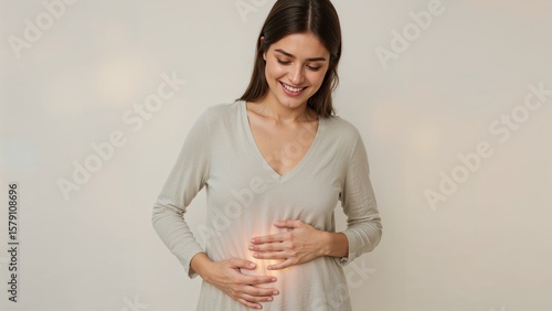 Smiling woman in a v neck shirt holding her stomach with a bright glow on her stomach area