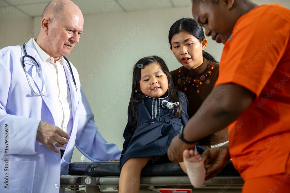 Obraz premium Little asian girl having accident with ankle sprain gets treatment from nurse and senior doctor in the hospital emergency unit with elastic bandage for healthcare and kid insurance concept