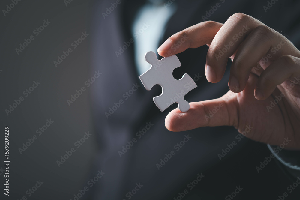 A person holds a single puzzle piece, symbolizing problem-solving and completion, set against a dark background. A person holds a single puzzle piece, symbolizing problem-solving and completion, set against a dark background.