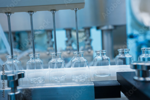 Close up of injection vaccine production machine manufacturing a lot of injections in glass ampoule vial in a healthcare pharmaceutical factory making process blue light with latest hi tech machinery	