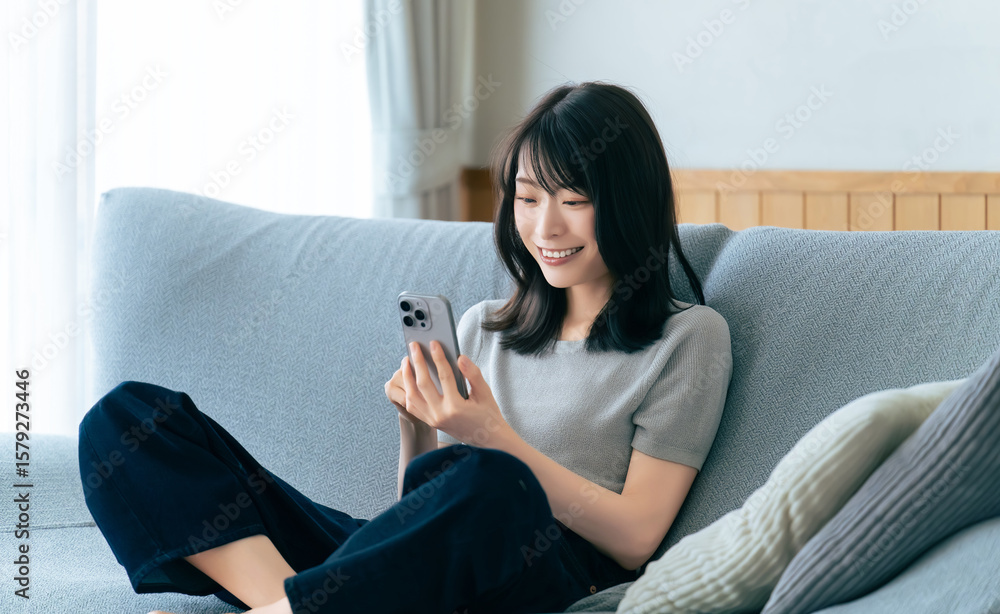 Obraz premium ソファに座ってスマートフォンを使う笑顔の女性