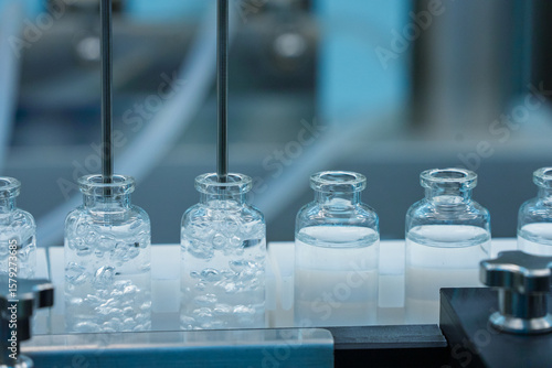 liquid injection filling line. vaccine production machine manufacturing a lot of injection in glass vial in a healthcare pharmaceutical factory making process blue light with hi tech machinery	
