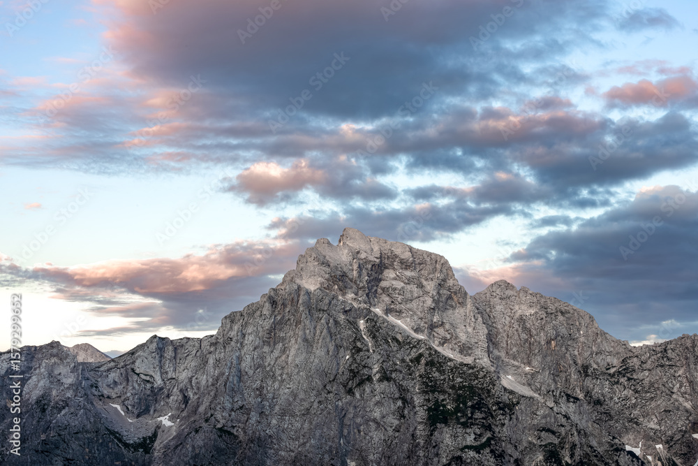 Fototapeta premium rugged mountain range under warm sunset light, with thick, moody clouds across the peaks. minimalist mountain background with empty space