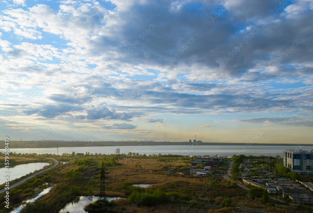 Fototapeta premium Picturesque scenery with a field and a lake under clouds at sunset