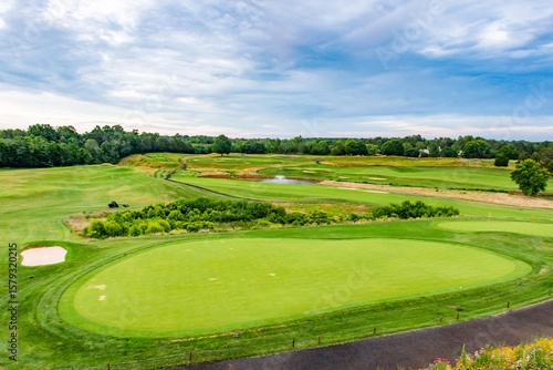Panoramic shot of a picturesque golf course in Charlottesville, VA. Emphasizes the strategic layout of the holes, featuring ponds and sand bunkers amidst rolling green hills.