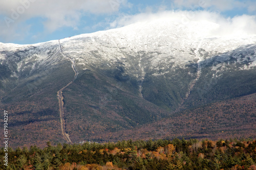Cog Railway tracks and Mount Washington in New Hampshire's scenic White Mountains. Trains can be seen climbing up tracks on distant ridge leading to snow covered summit.