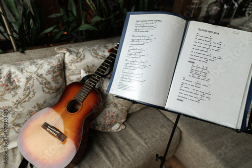 Bild auf Leinwand Acoustic guitar next to an open songbook on a cozy couch with floral pillows