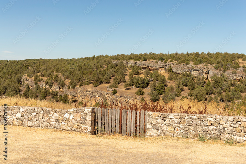 Fototapeta premium a stone wall with a double wooden gate in the center and a mountainous landscape in the background