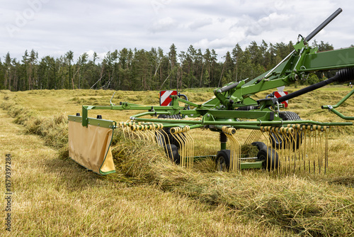 Making hay with the hay tedder. Farm Machine Tractor With Rotating Rake Attachments. Close Up Shot. Tractor with tedder shaking mowed grass.