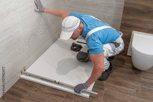 Installation of bathroom equipment. A worker measures the horizontality of a shower tray.