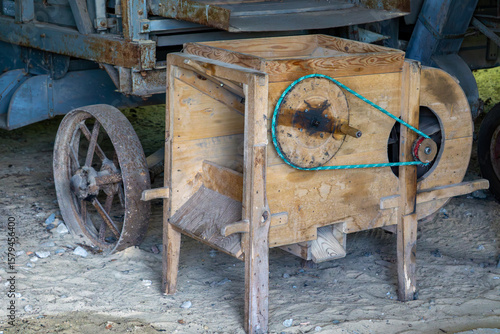 Vintage wooden grain winnower with a pulley wheel, used for cleaning harvested grain. Traditional agricultural machine from a rural farm setting.