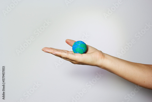 Hand presenting miniature Earth globe on open palm against neutral background, representing environmental care and responsibility. Environmental conservation concept. Humanitarian aid an global unity.
