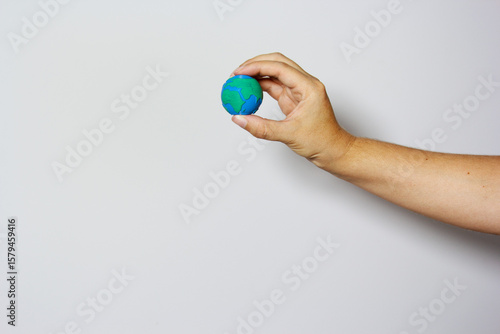 Single hand delicately grasping small Earth globe with fingers against neutral background, symbolizing environmental protection and care. Earth day concept. Environment day. 
