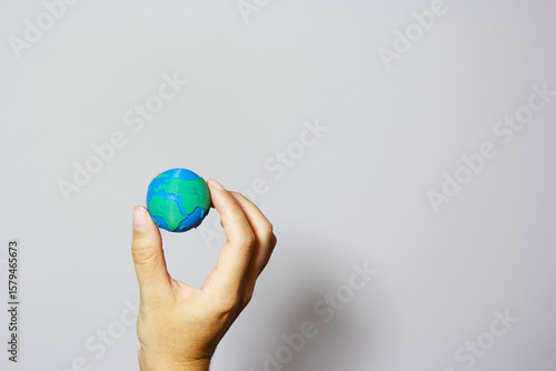 Single hand forming protective cup around miniature Earth globe against neutral background, symbolizing environmental care and global protection. Earth day concept. Responsible business. 