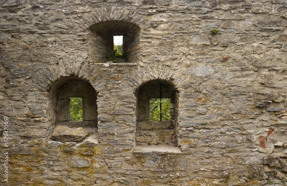 Naklejka premium Small arched windows in the stone wall of the castle. Arched windows of the walls. View of the surroundings, peephole for defending archers. Texture of the stone wall. Exploring Czech monuments.